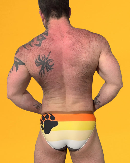 Man wearing colorful swim briefs with a bear paw design on a yellow background