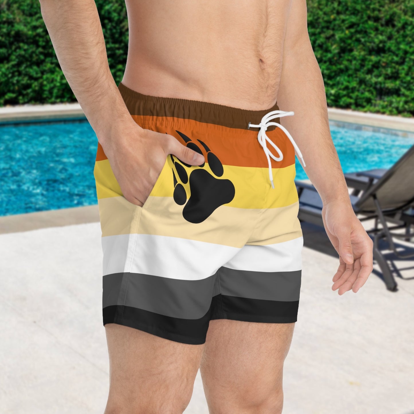 A person wearing striped pride flag swim shorts with a bear paw print design by a pool.