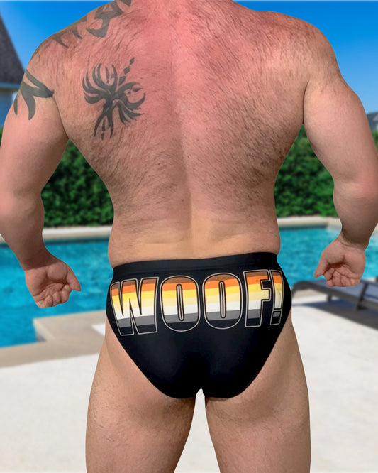 Muscular man wearing black speedo with gay bear pride flag "WOOF" 