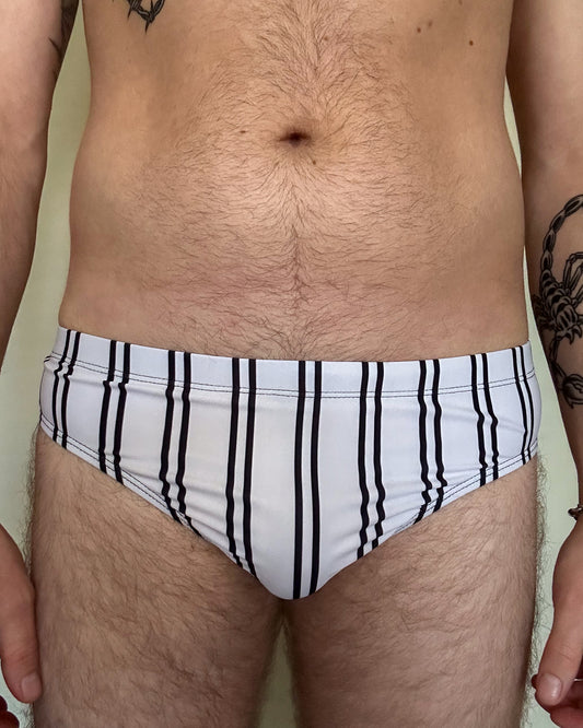 Person wearing a white swim brief with black stripes against a plain background